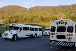 Young Transportation activity buses staged on a lot with wooded mountains behind
