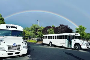 Two Young Transportation activity buses parked in a lot under a rainbow