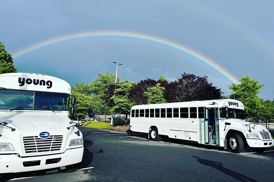 Two Young Transportation activity buses parked in a lot under a rainbow