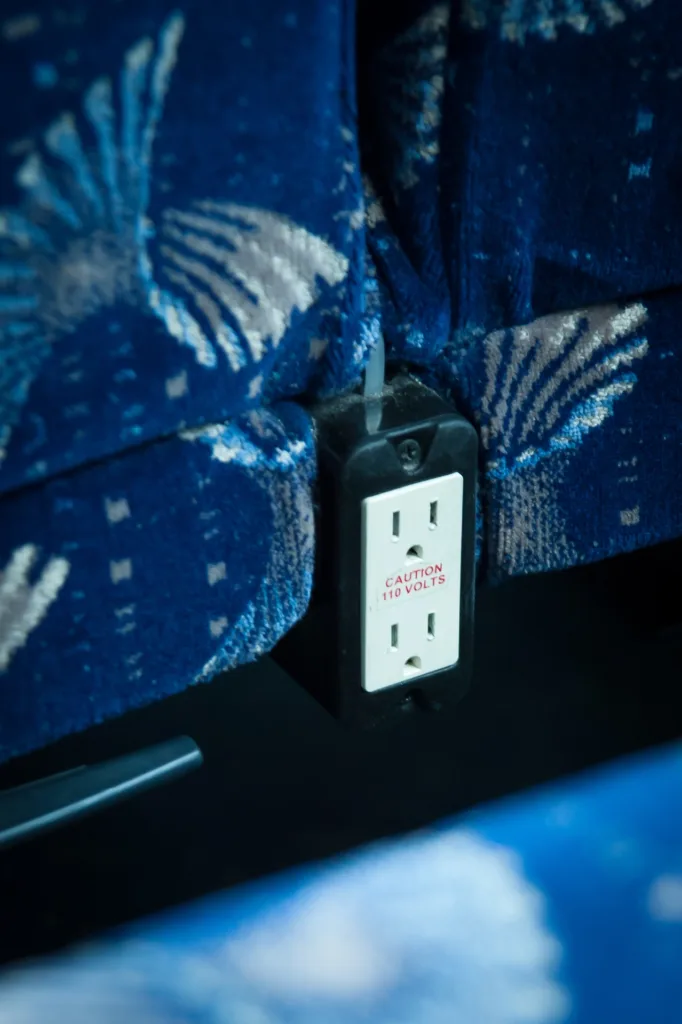 110-volt power outlet mounted between motorcoach seats, labeled Caution 110 Volts