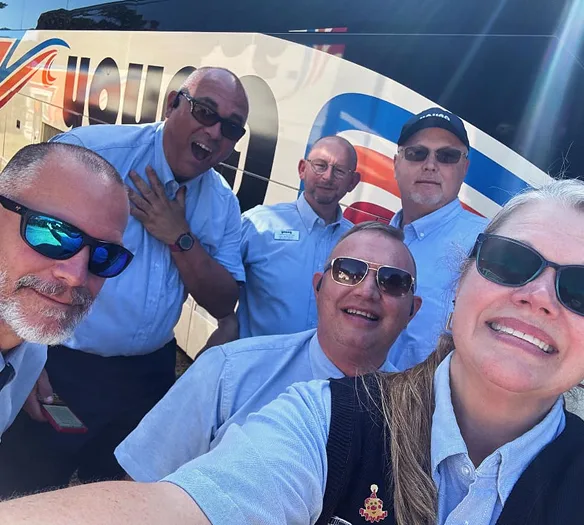 Five Young Transportation drivers and staff smiling in front of a motorcoach in uniform