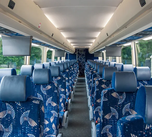 Motorcoach interior with rows of blue patterned seats, overhead monitors, and center aisle