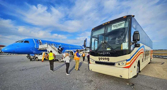 Passengers boarding a Young Transportation motorcoach beside a team charter aircraft