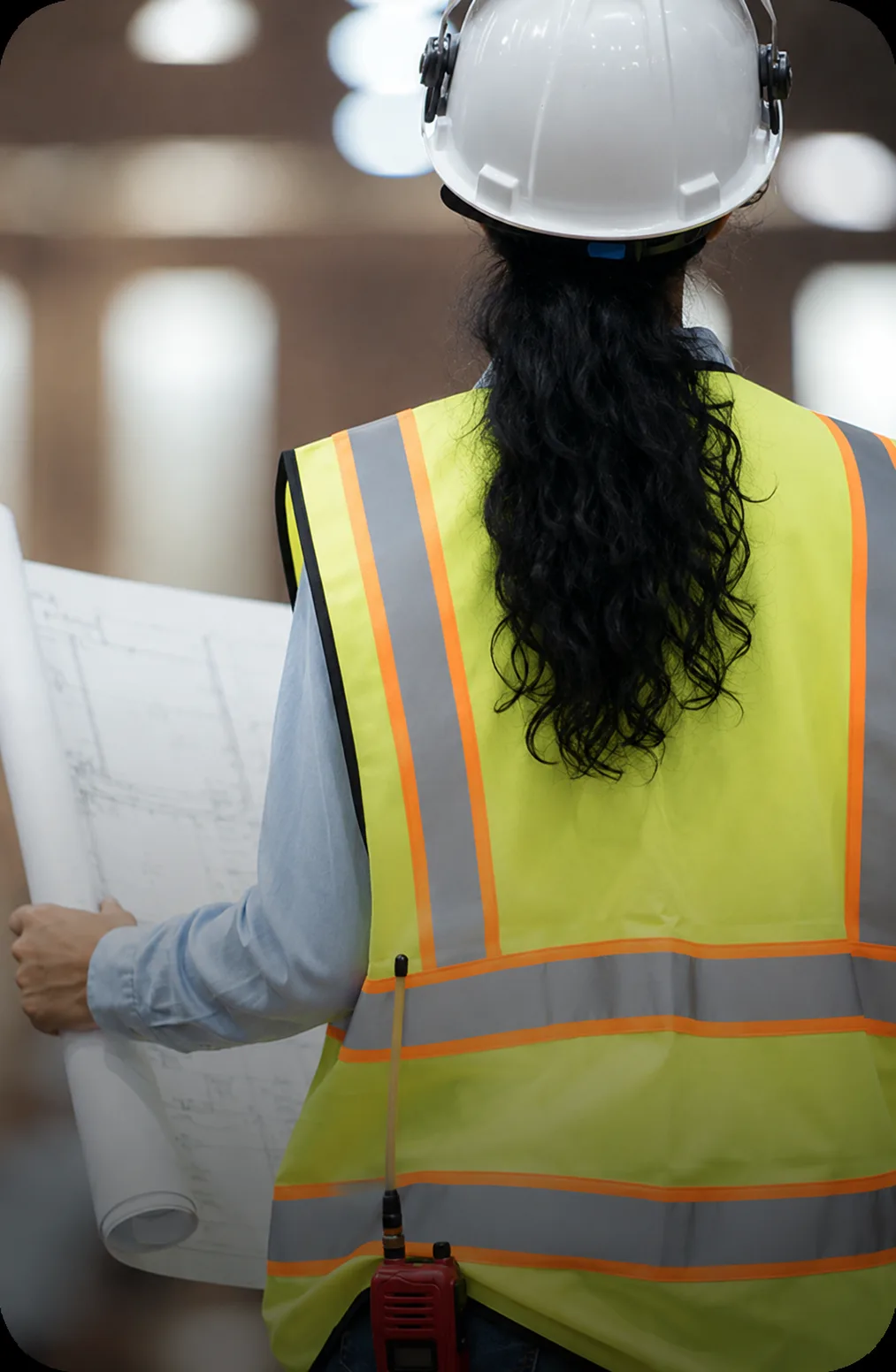 Construction worker in a hard hat and safety vest holding blueprints inside a facility