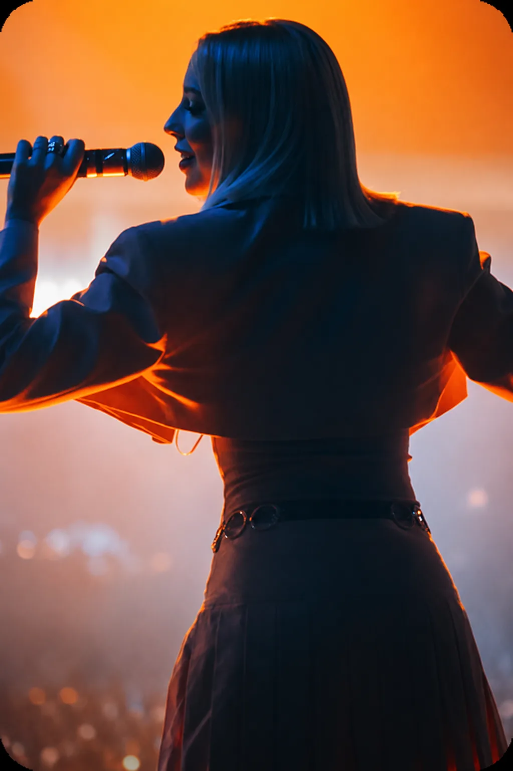 Female performer singing into a microphone on stage, bathed in warm orange stage lighting